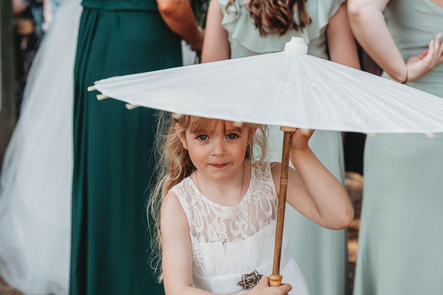 Young person in white lace dress holds delicate white parasol during outdoor celebration.