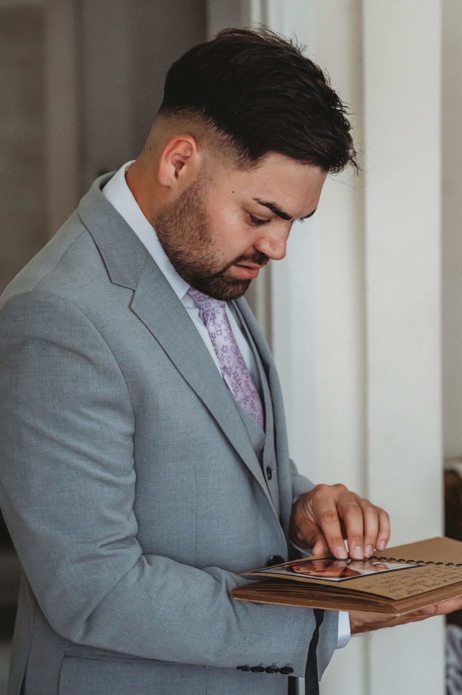 Person in light gray suit and purple tie looks down while holding a document on a clipboard.