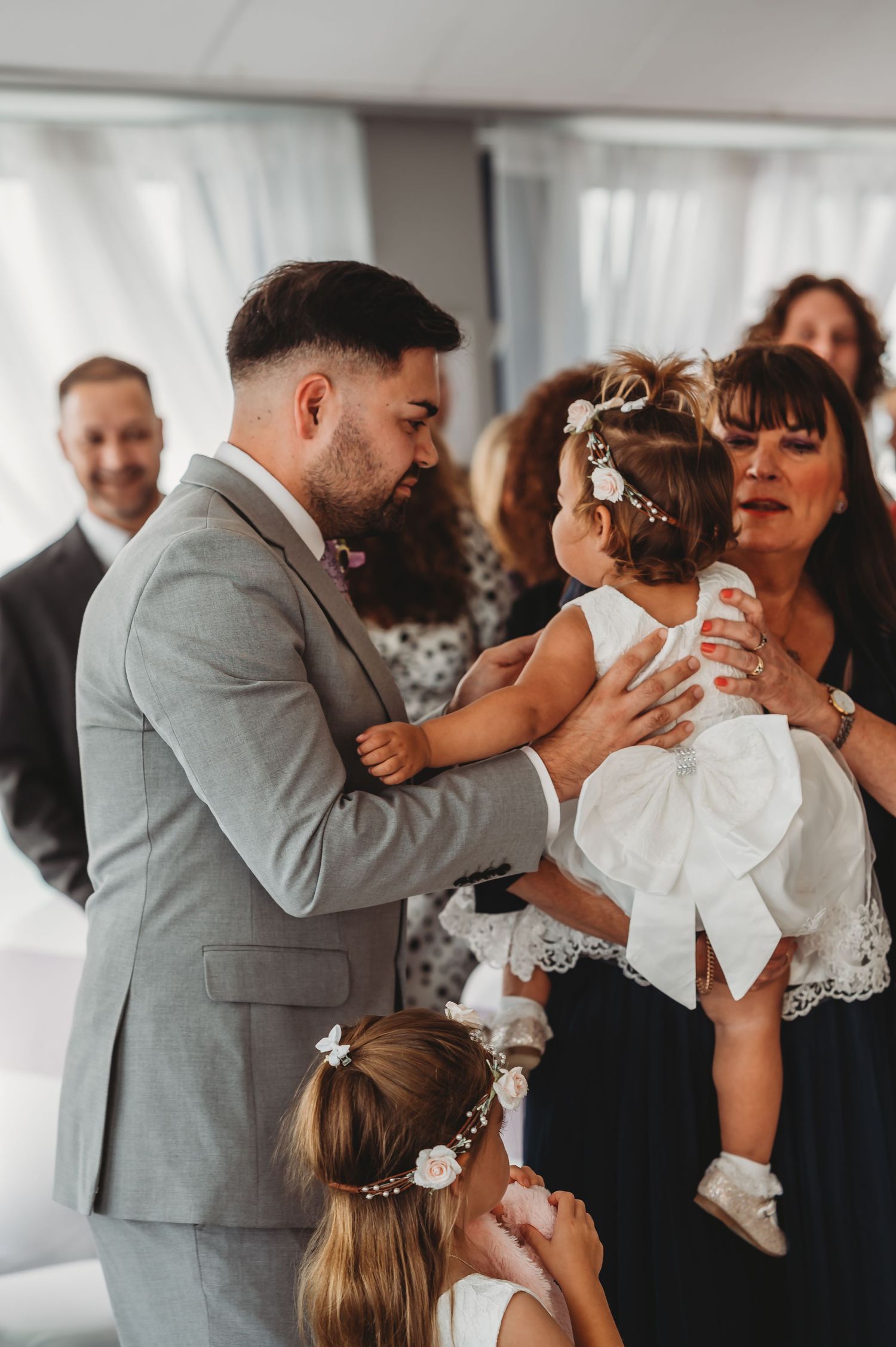 A tender moment shared with a young flower girl in a white dress during an indoor wedding celebration.