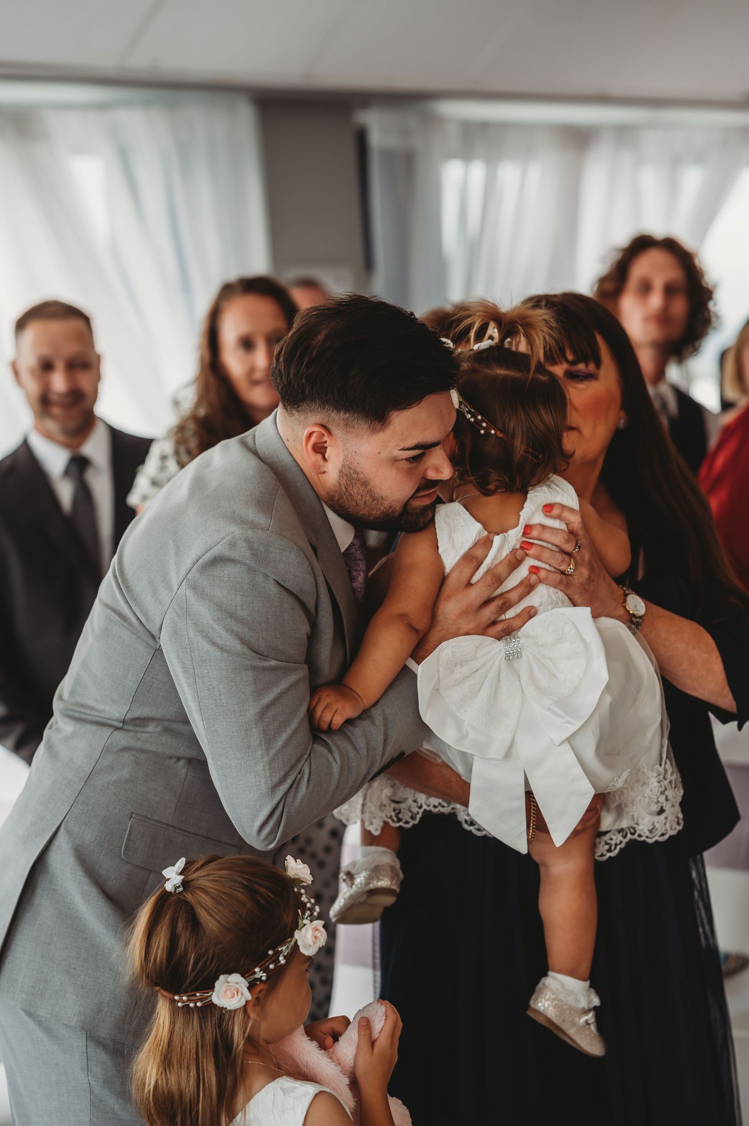 A touching moment at a wedding celebration shows a tender embrace between the couple while holding a small child in white.