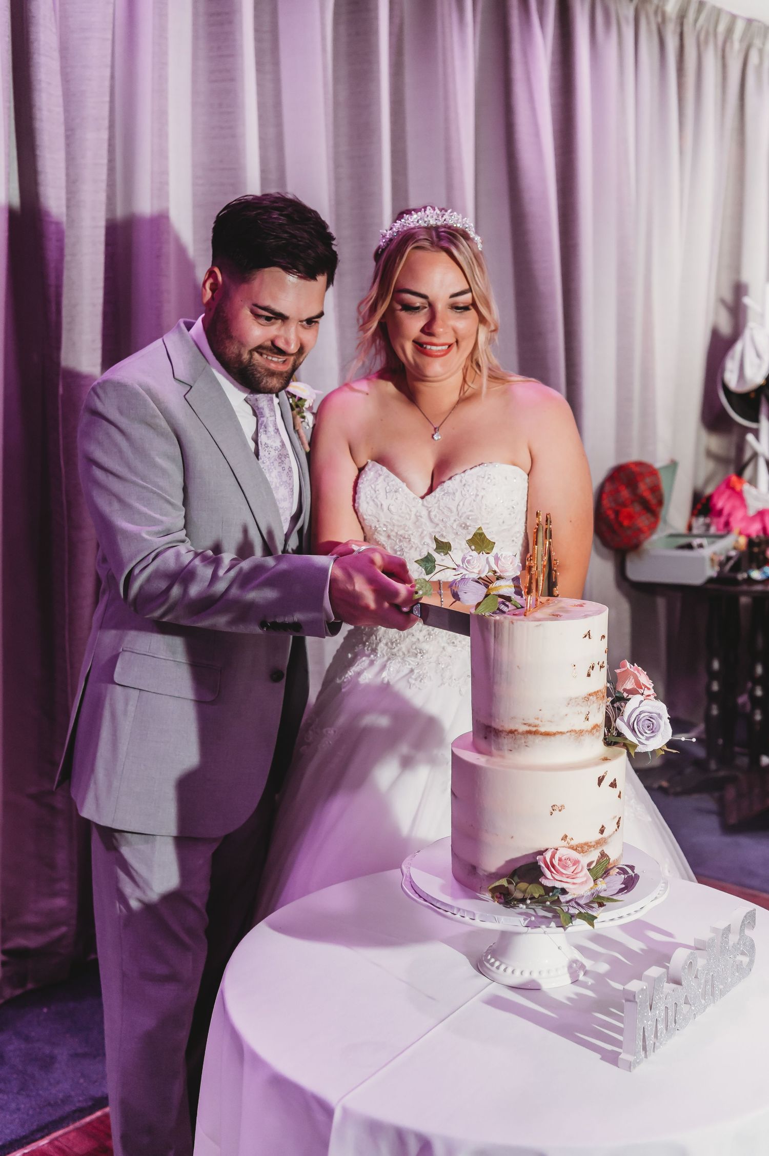 Traditional wedding cake cutting moment with elegant tiered cake decorated with flowers.
