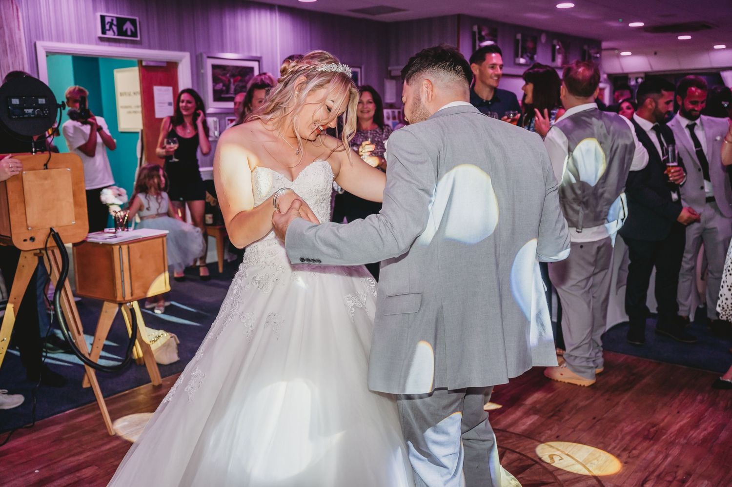 Bride and groom share their first dance together on the wooden dance floor at their wedding reception with purple lighting.