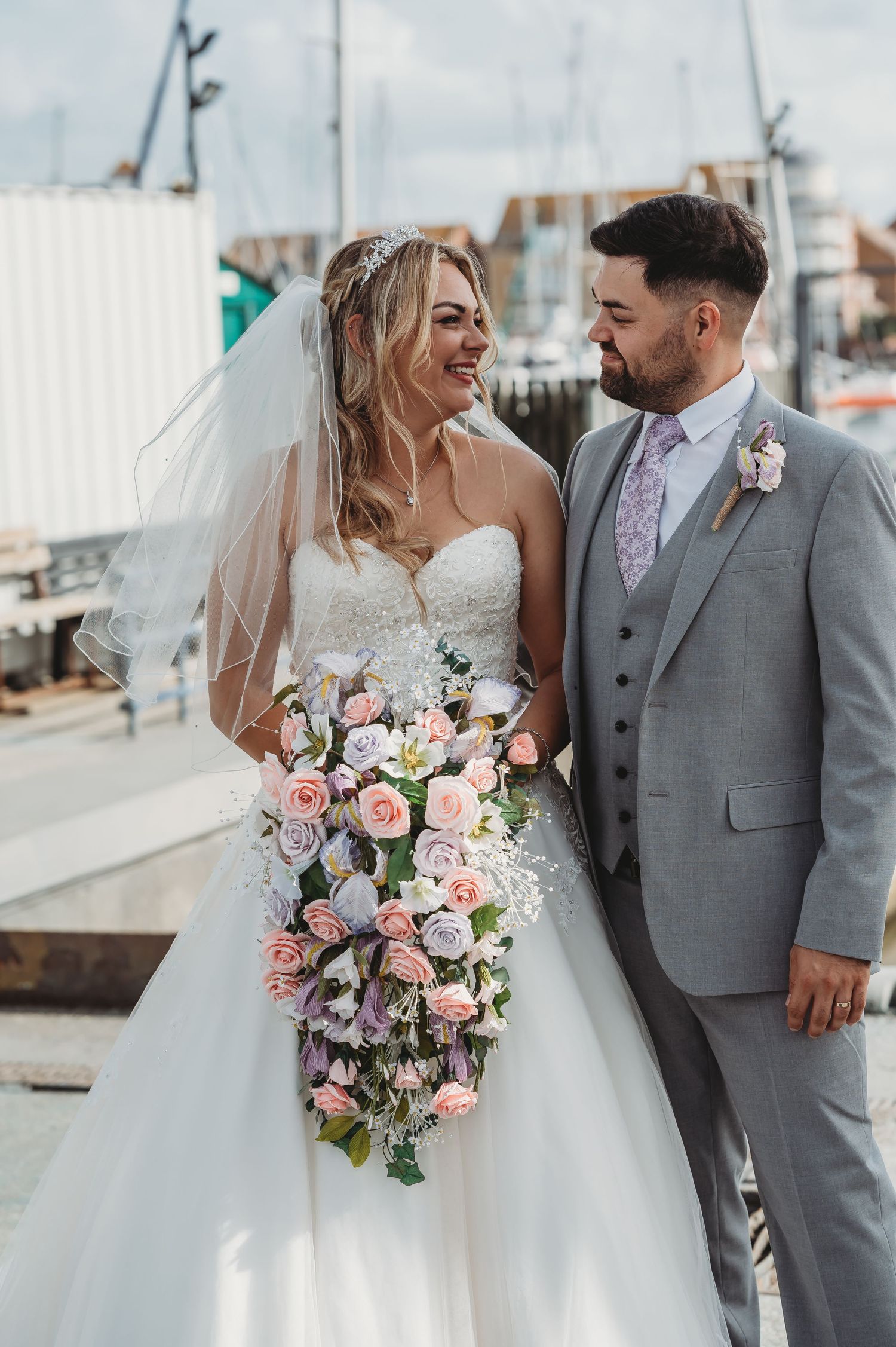 Waterfront wedding portrait with bride holding cascading pink and purple bouquet by marina.