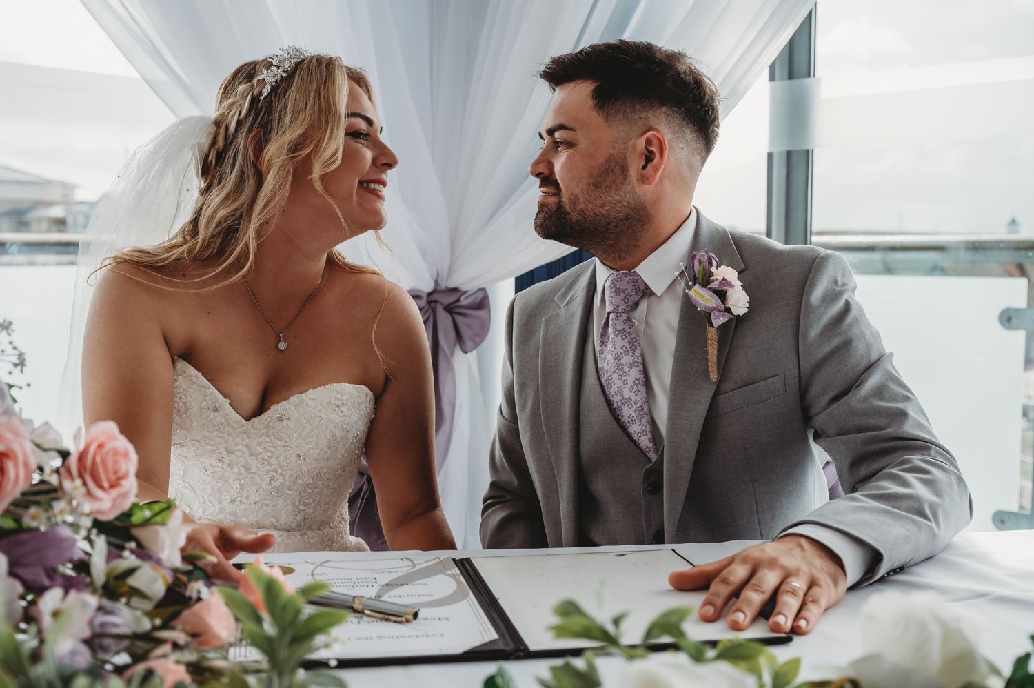 Two people share a joyful moment while seated at a table decorated with floral arrangements at an elegant event.