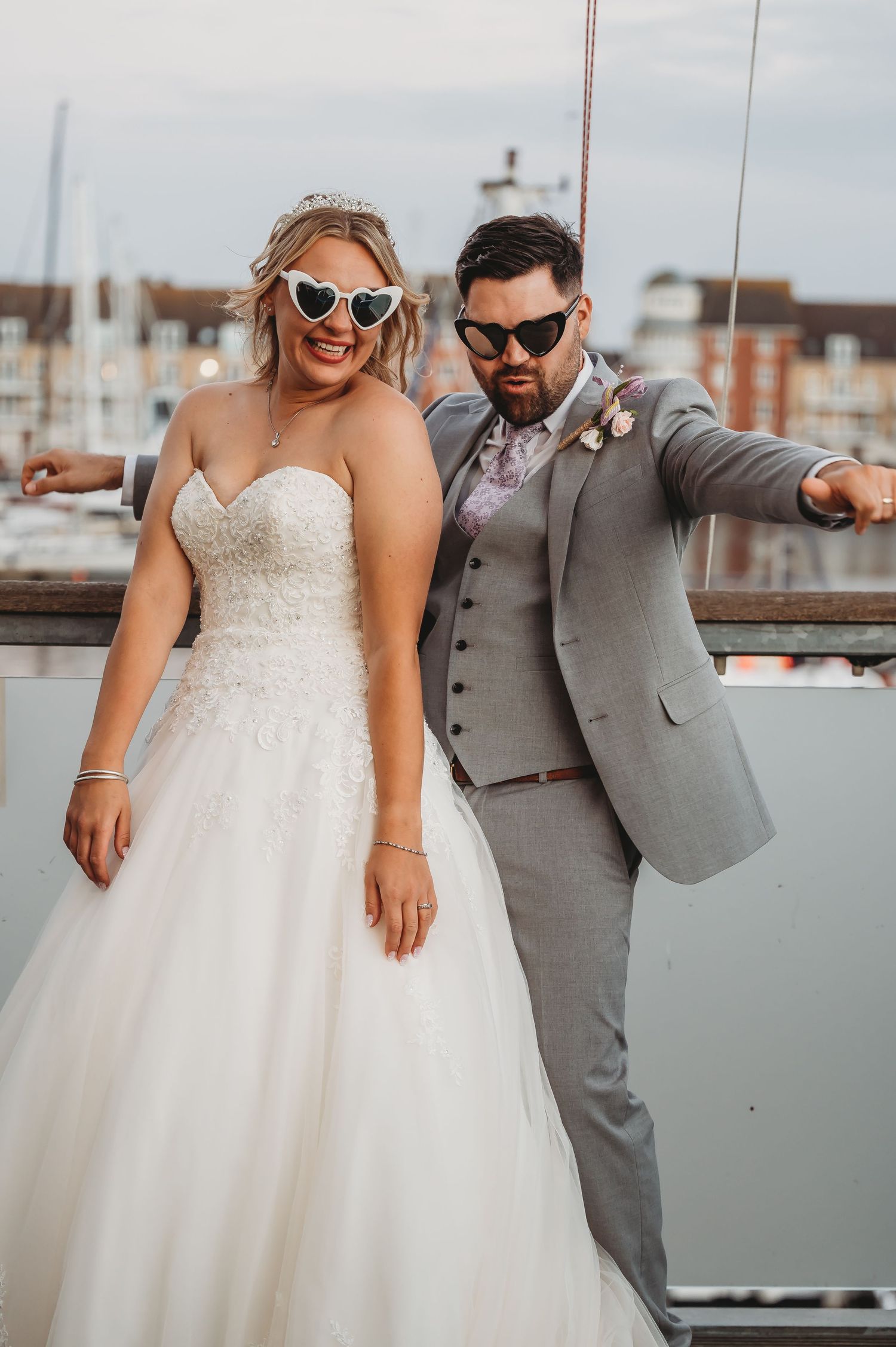 A celebratory wedding portrait captures a couple in sunglasses and formal attire at a waterfront location.