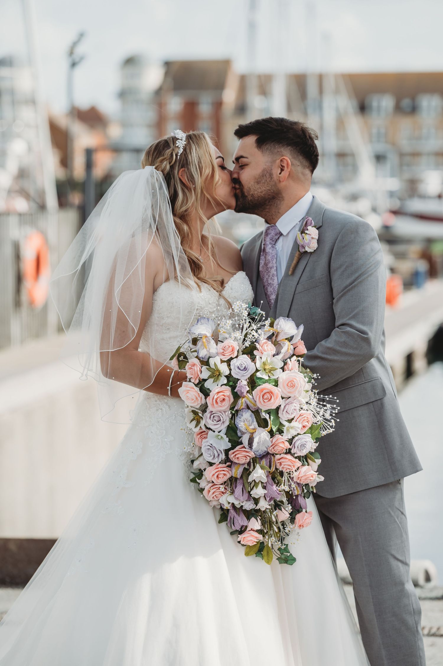 Romantic waterfront wedding photo with elegant white dress, gray suit and cascading pink floral bouquet by marina.