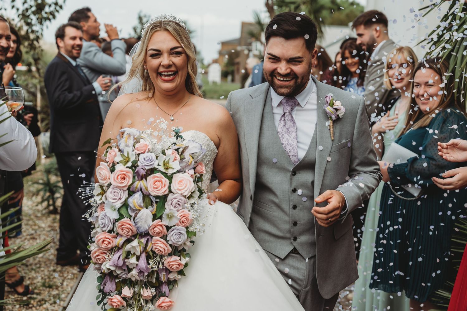 A joyful couple walks together after their wedding ceremony while guests throw confetti in celebration.