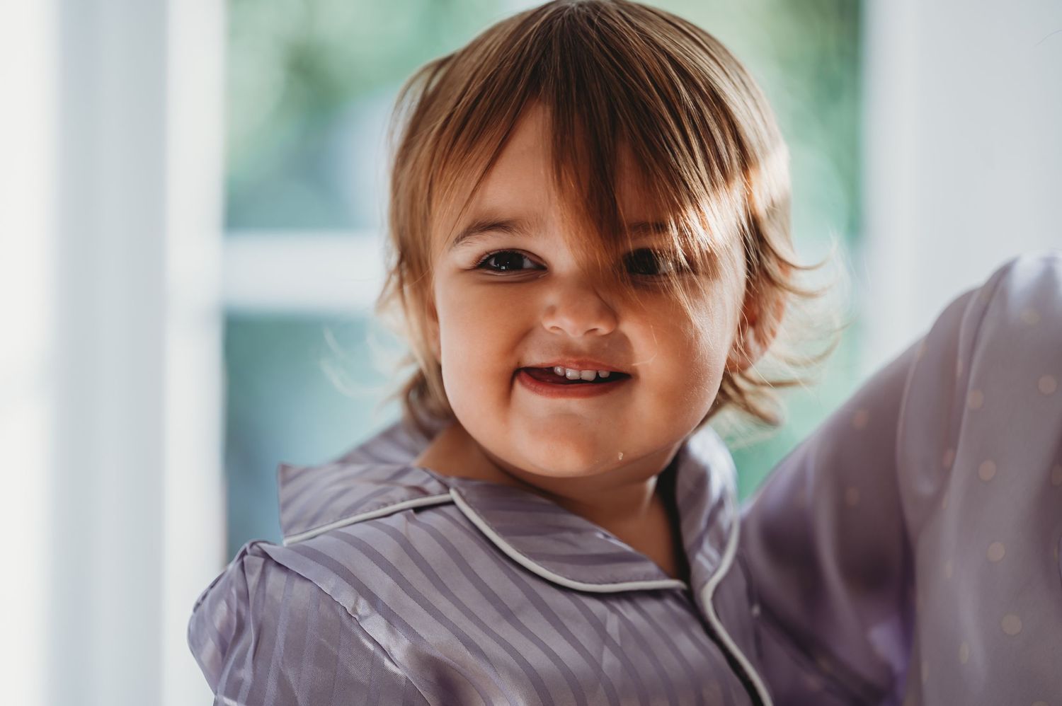 A happy child wearing a gray shirt smiles with bright joy.