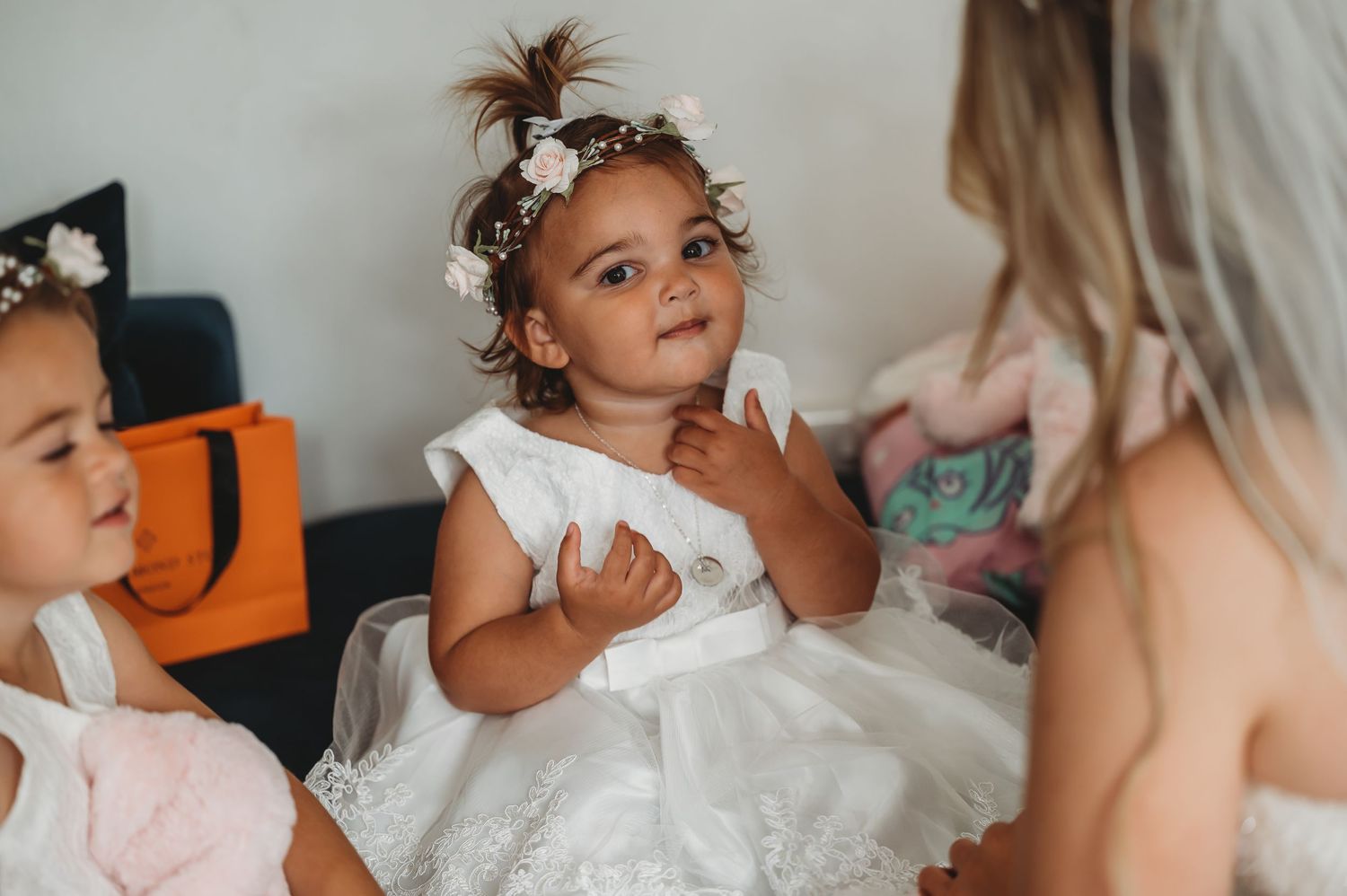 Young girl in a white dress and floral hair accessories sits attentively during a special celebration gathering.