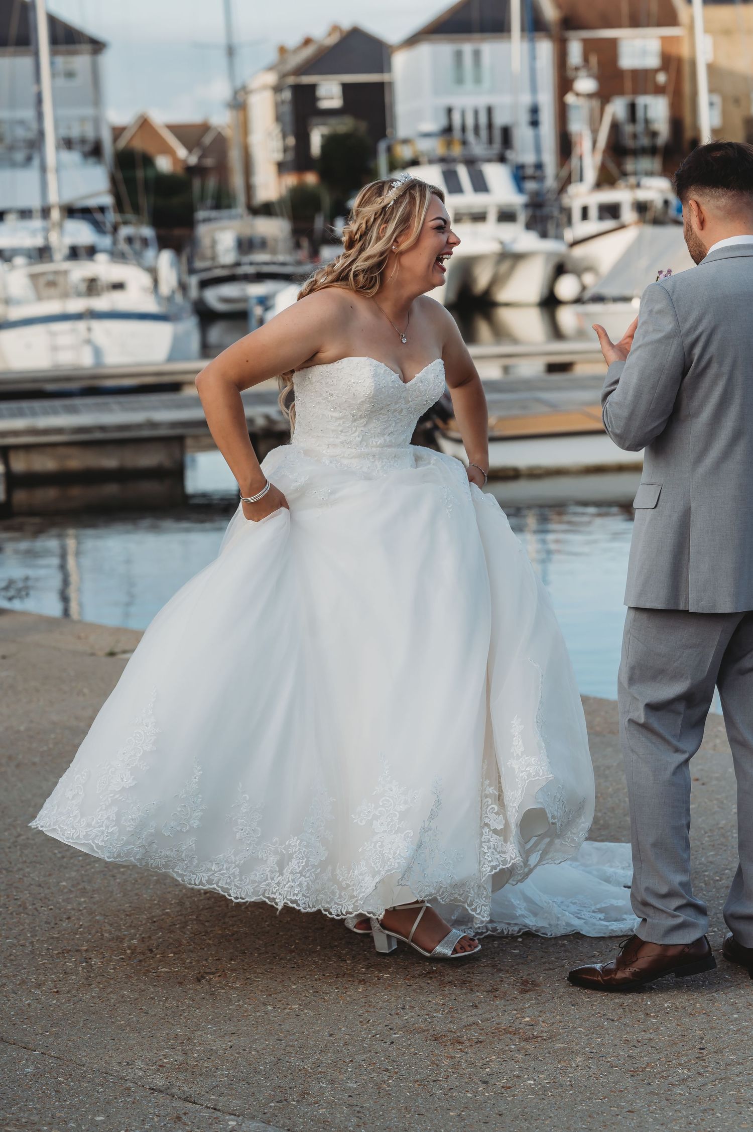 A wedding couple stands at a marina with boats in the background as the bride wears a stunning white strapless ballgown.