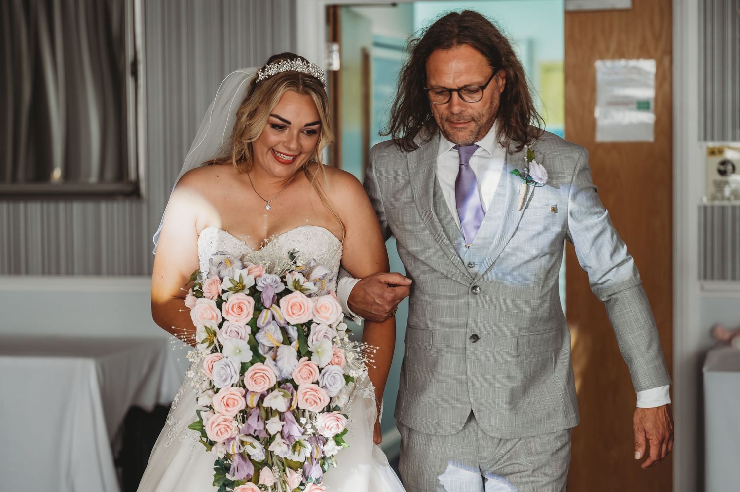 Happy couple celebrates their special day in intimate indoor setting with pink and lavender floral bouquet.