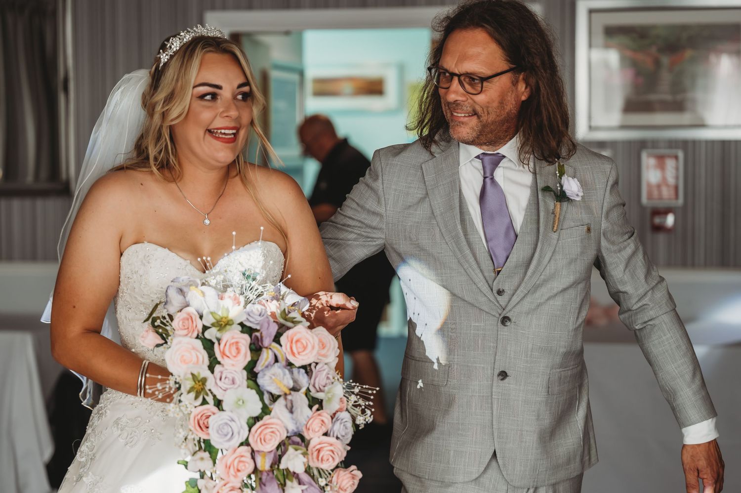 A happy couple on their wedding day share a joyful moment, with the bride holding a pink and white bouquet.