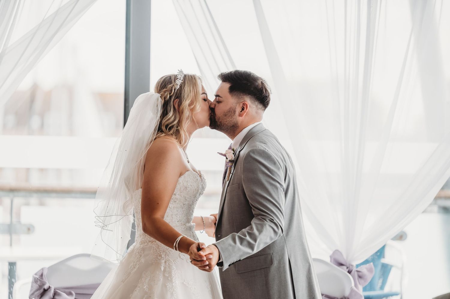 A bride and groom share a tender kiss under flowing white curtains during their elegant wedding ceremony.