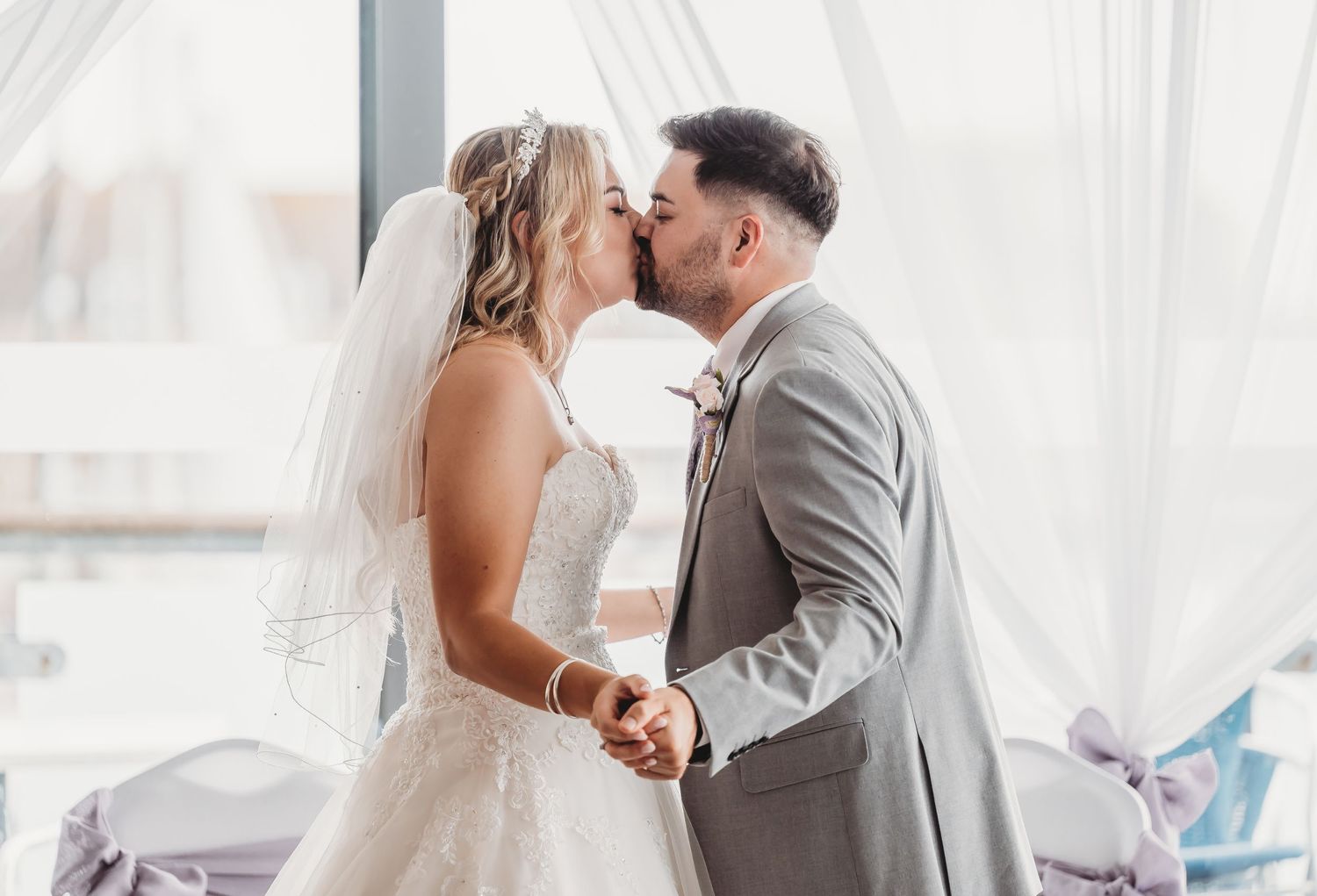 A bride and groom share their first kiss as a married couple under flowing white curtains at their wedding ceremony.
