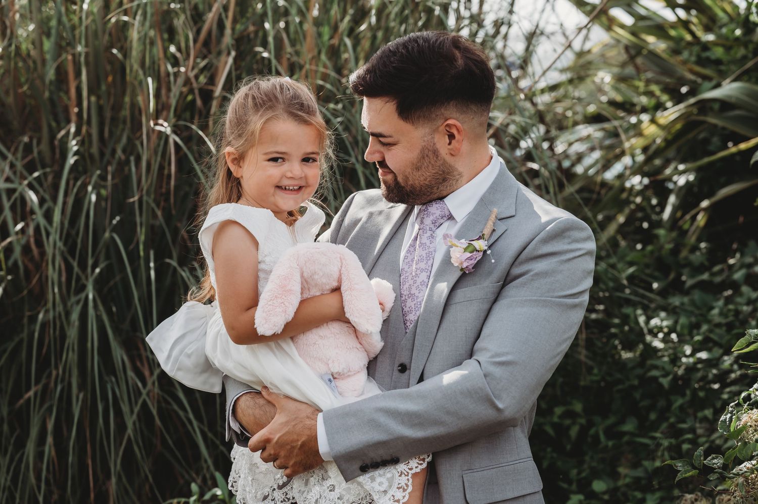 A heartwarming moment between a well-dressed man in a gray suit and a young girl in a white dress outdoors.
