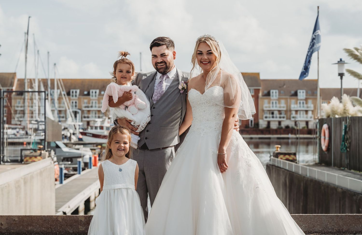 A wedding party poses together on a dock with boats and a marina in the background.