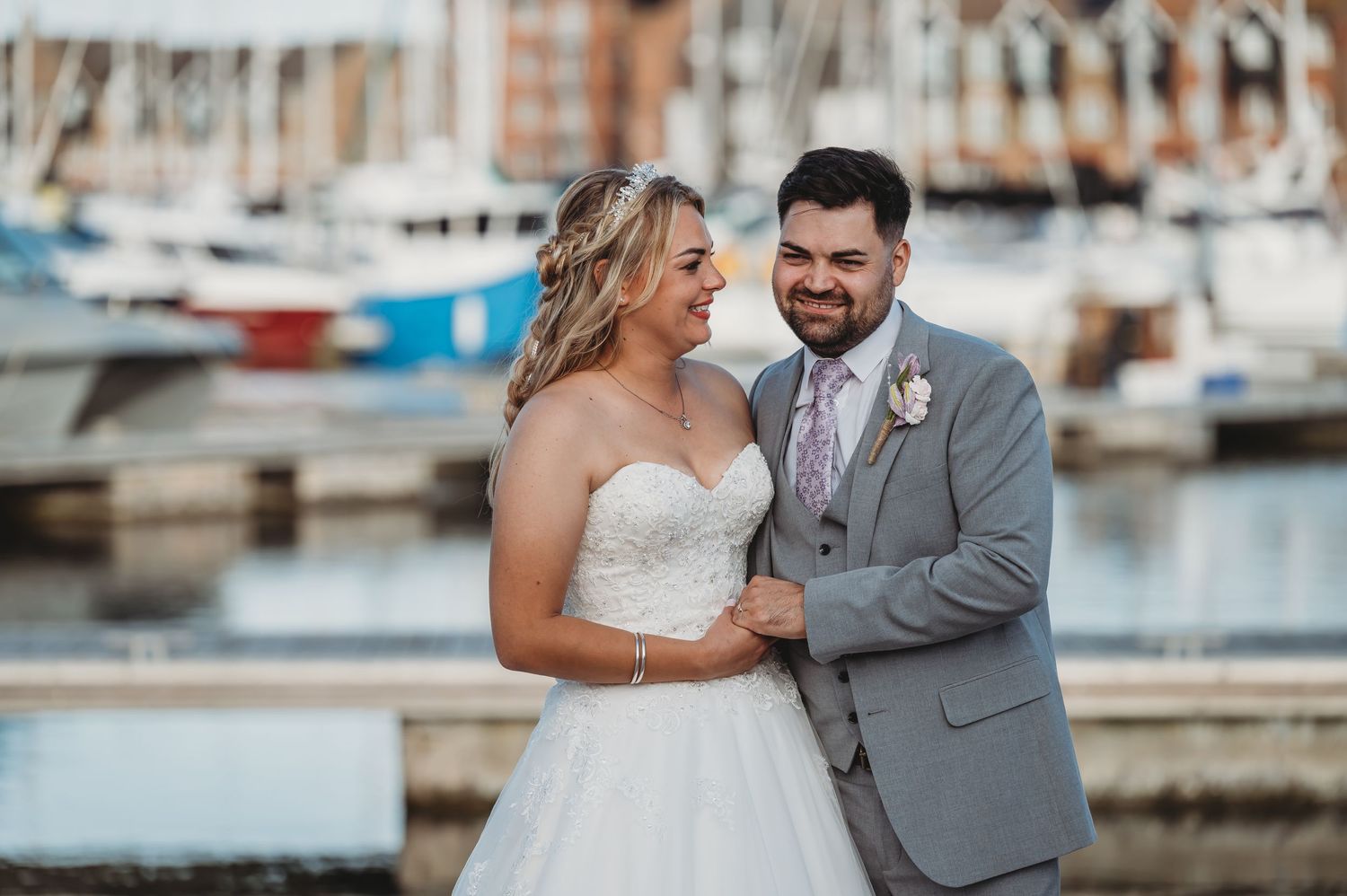 A joyful newlywed couple sharing a romantic moment by the marina with boats in the background at sunset.