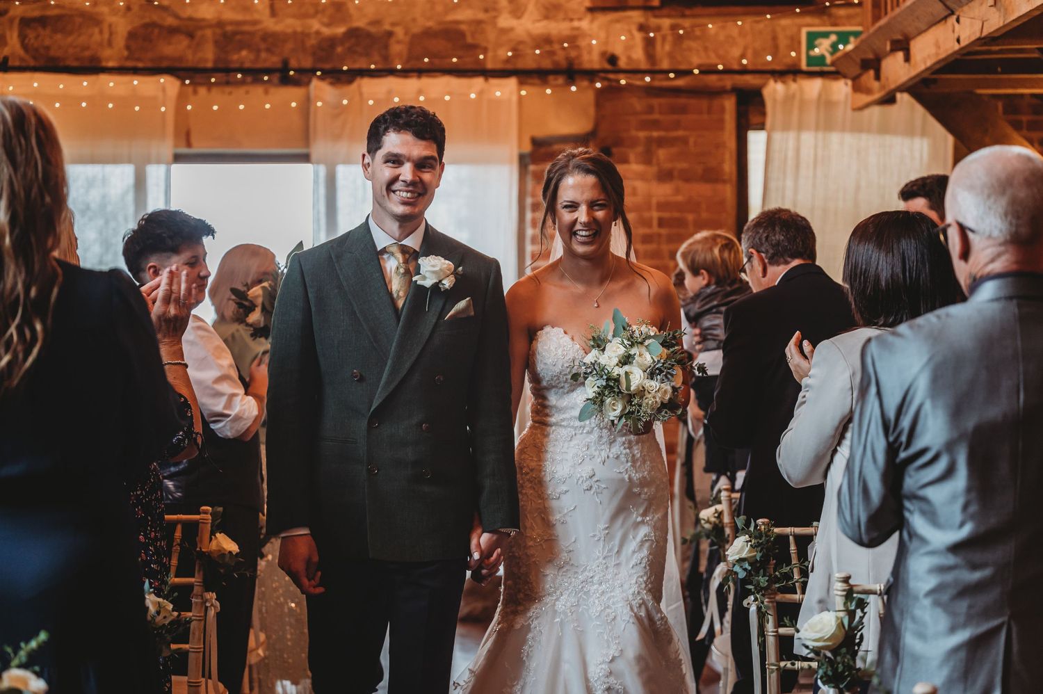 A wedding ceremony in a rustic indoor venue with exposed brick walls and string lights.