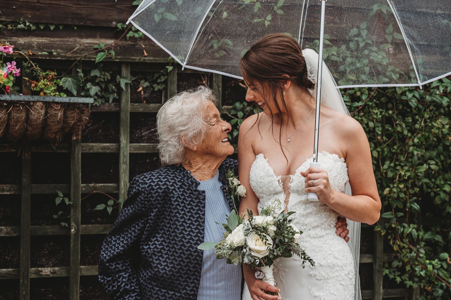 A heartwarming moment shared between a bride and an elderly woman under a clear umbrella.