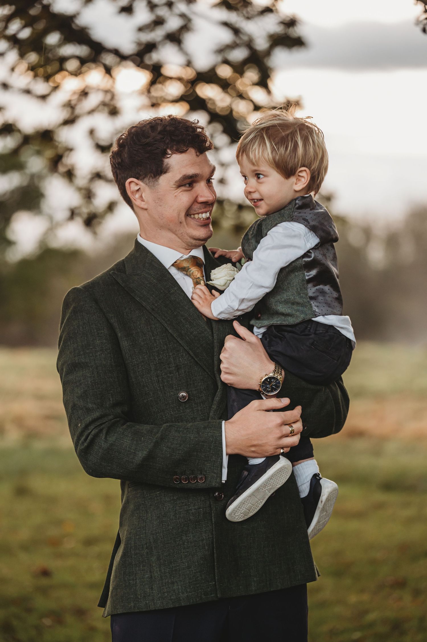 Candid outdoor portrait of a parent in dark wool coat holding young child against autumn background.