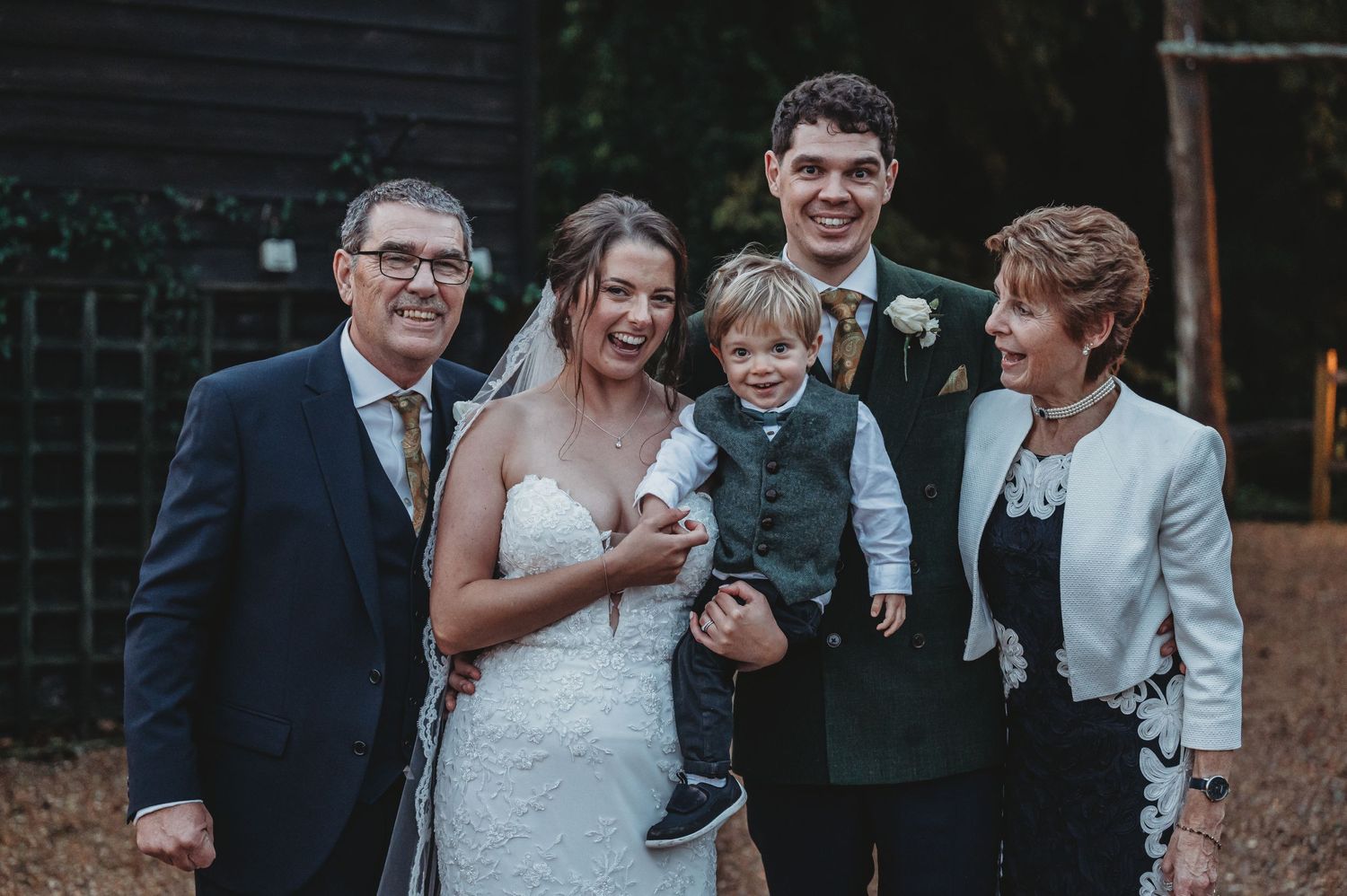 Family gathering at outdoor wedding with young child against dark building.