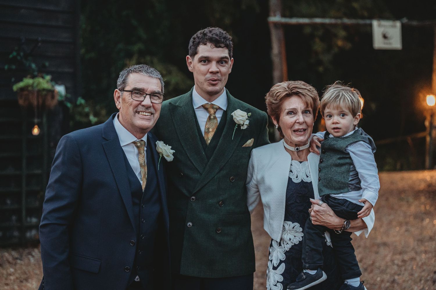 Formal wedding party portrait with small child against dark rustic backdrop.