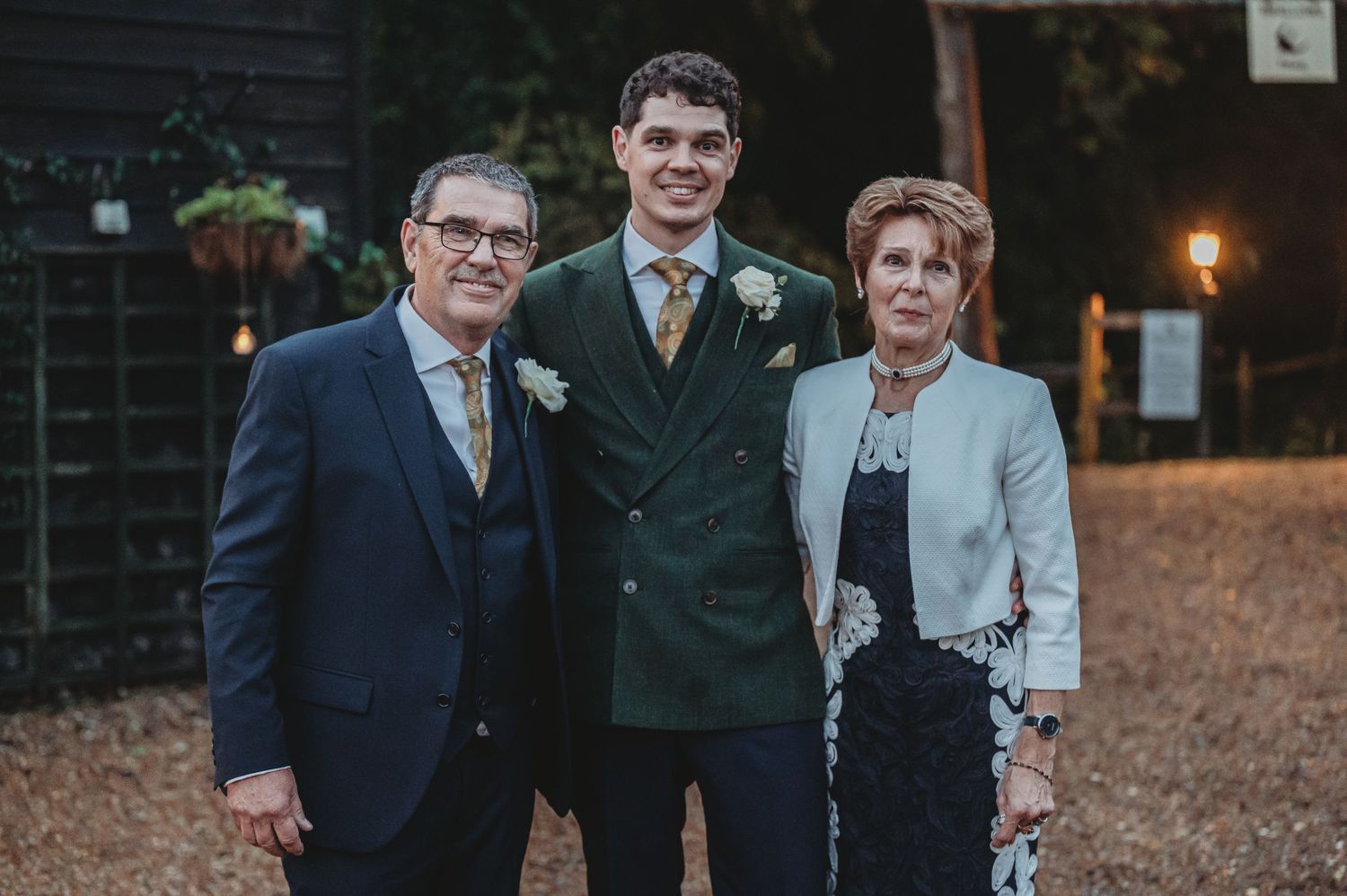 Family members pose together at evening wedding reception with dark building backdrop.
