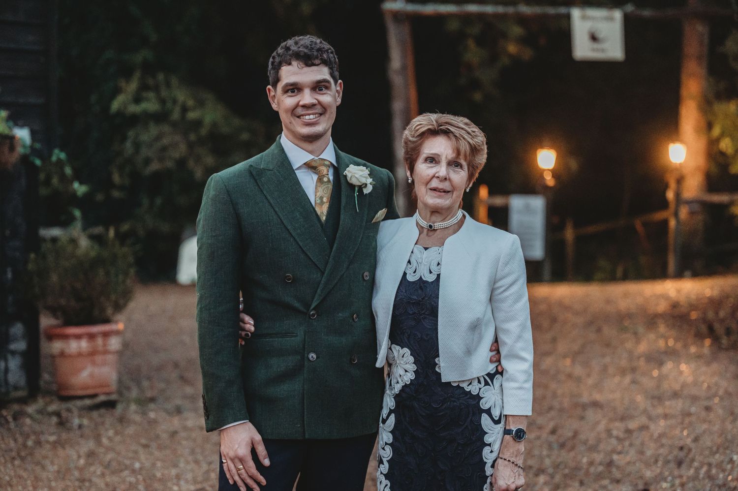 Elegant evening wedding portrait with guests in formal attire against dark outdoor setting.
