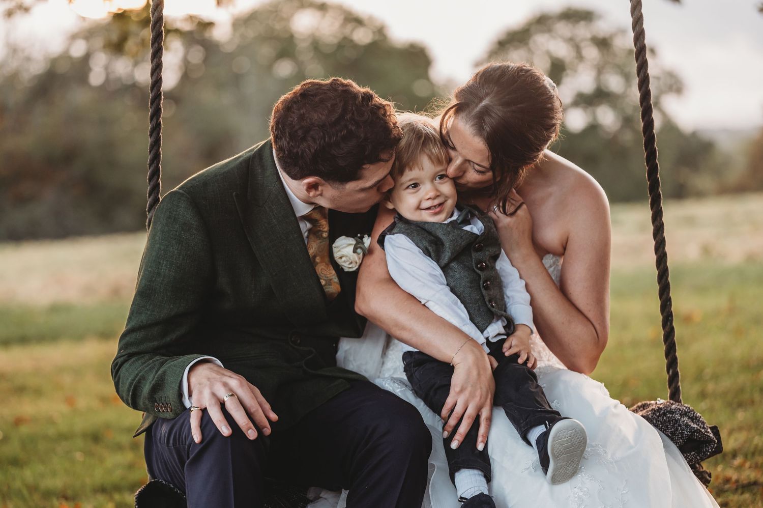 A joyful family moment together on a rustic rope swing at sunset in a grassy field.