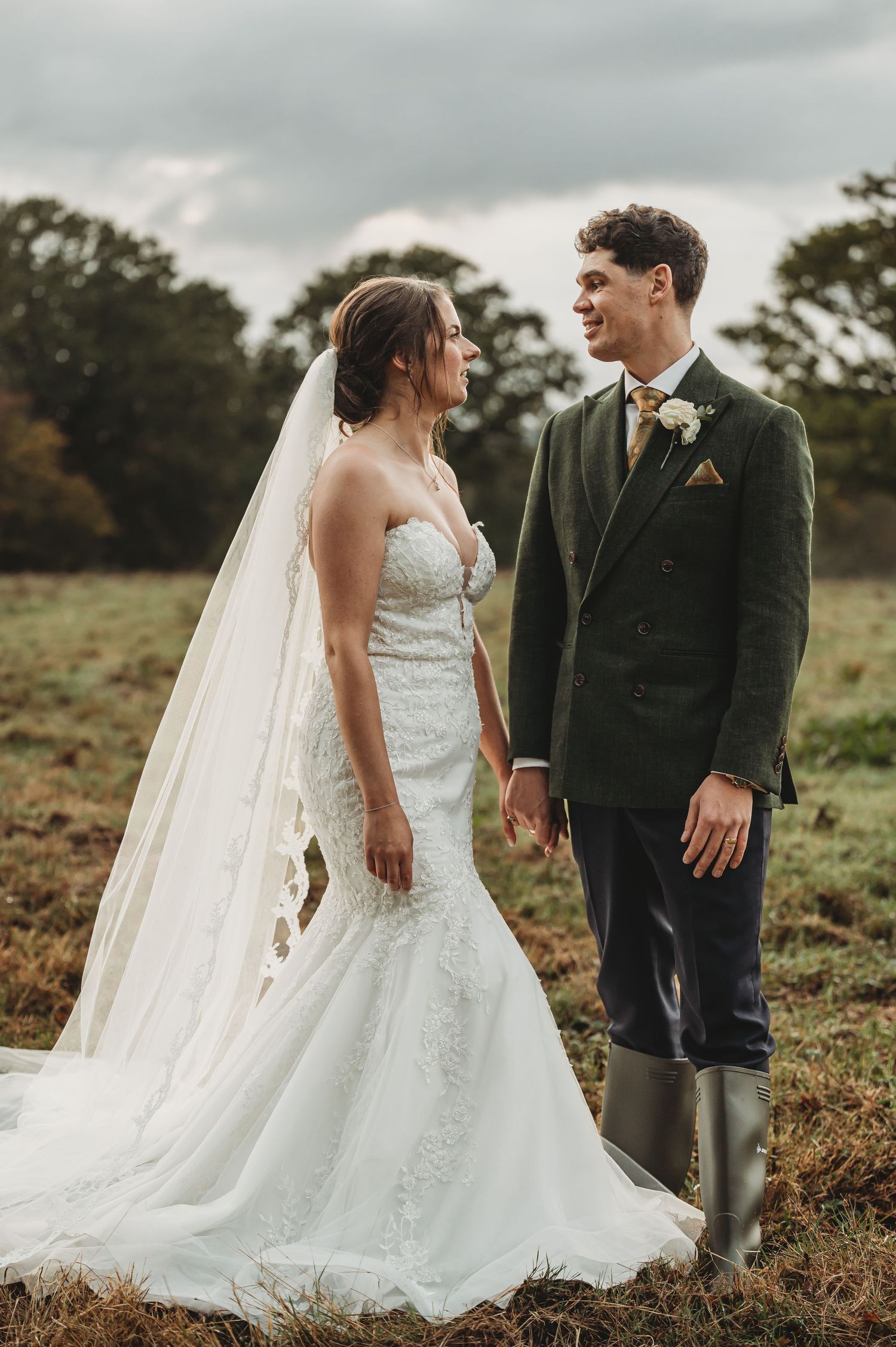 A couple shares a joyful moment in a field during their rustic wedding, the groom wearing rain boots with his suit.