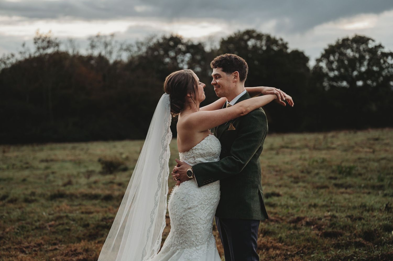 Romantic outdoor wedding embrace with cloudy sky and rolling hills in background.