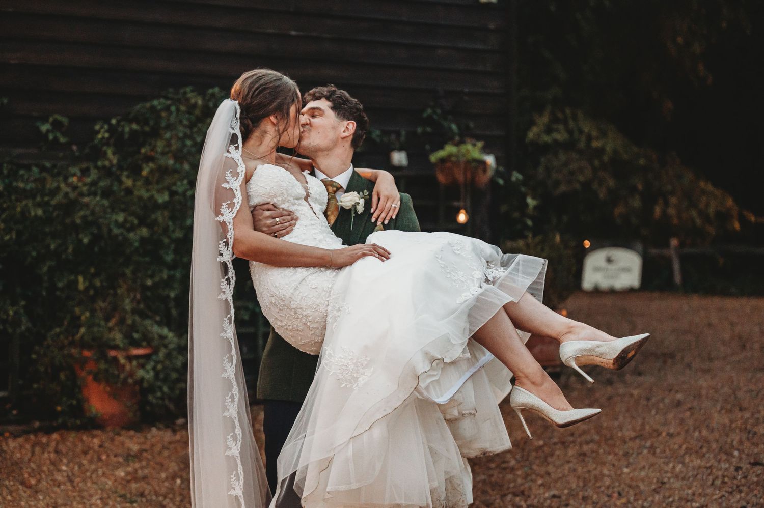 An intimate wedding couple embraces in a romantic pose outdoors with the bride wearing a white dress and heels.