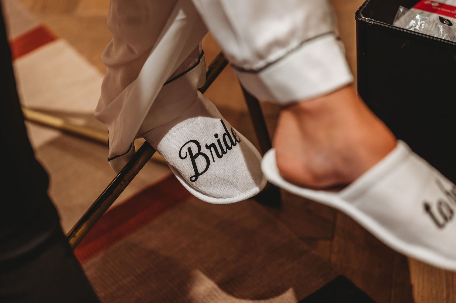White bridal slippers with 'Bride' text shown on hardwood floor during wedding preparation.