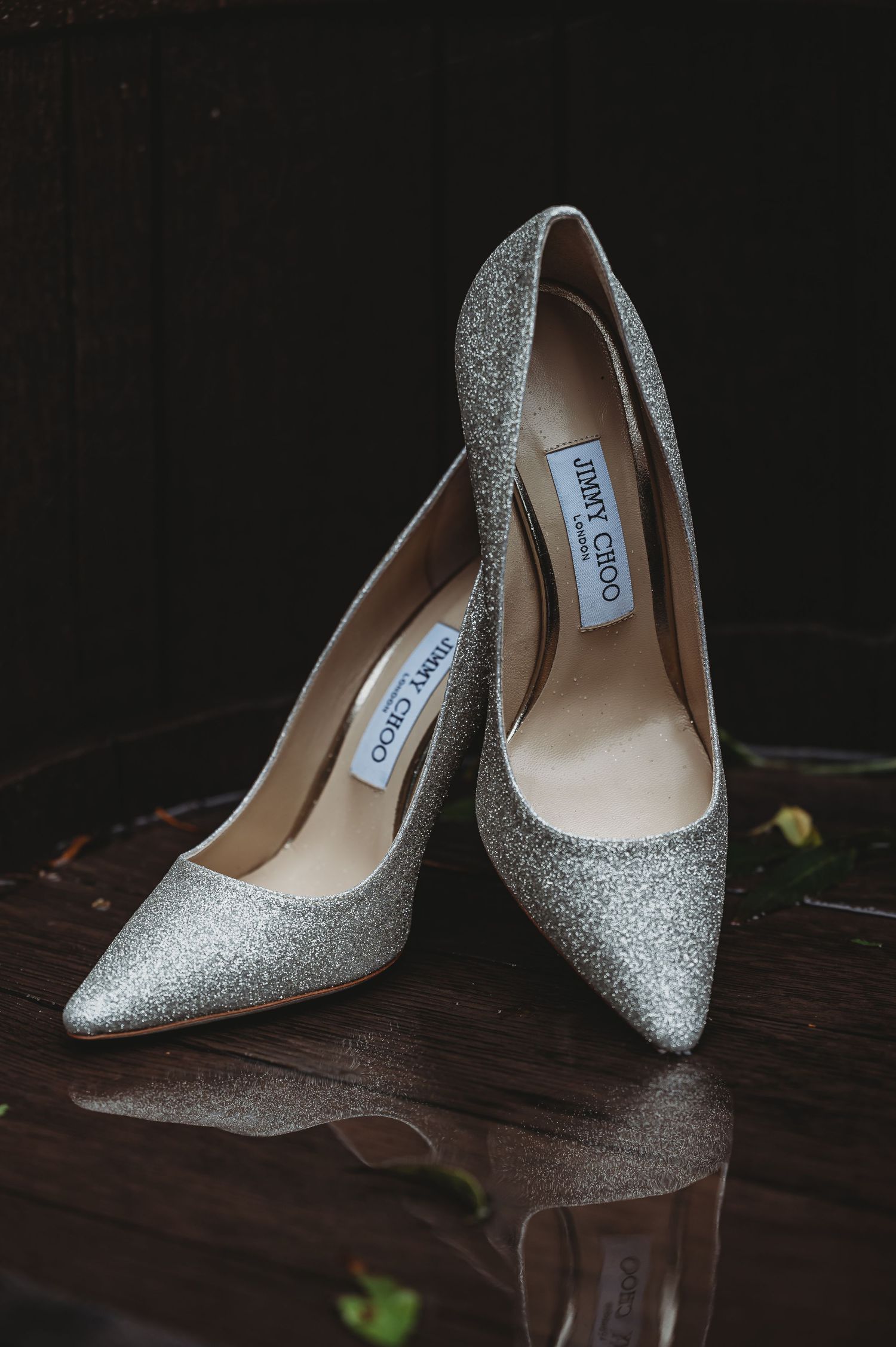 Sparkly silver Jimmy Choo stiletto heels on a dark wooden surface.
