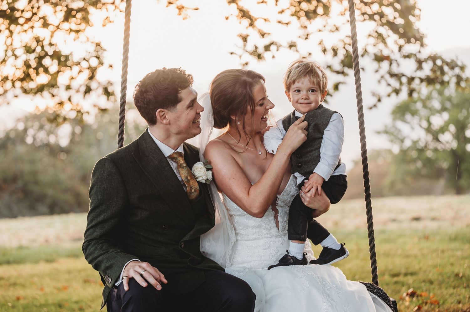 Family moment captured on a wooden swing during sunset after a wedding ceremony.