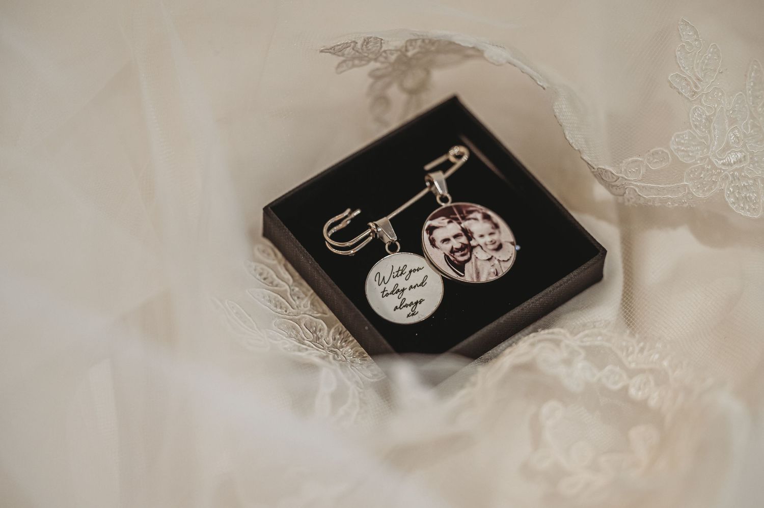 A small black box contains two engraved silver pendant charms on a white fabric background.