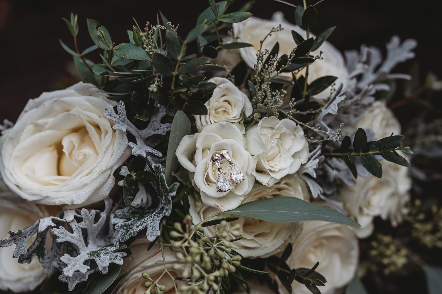An elegant bridal bouquet featuring cream roses, dusty green eucalyptus, and silvery foliage arranged in a romantic style.