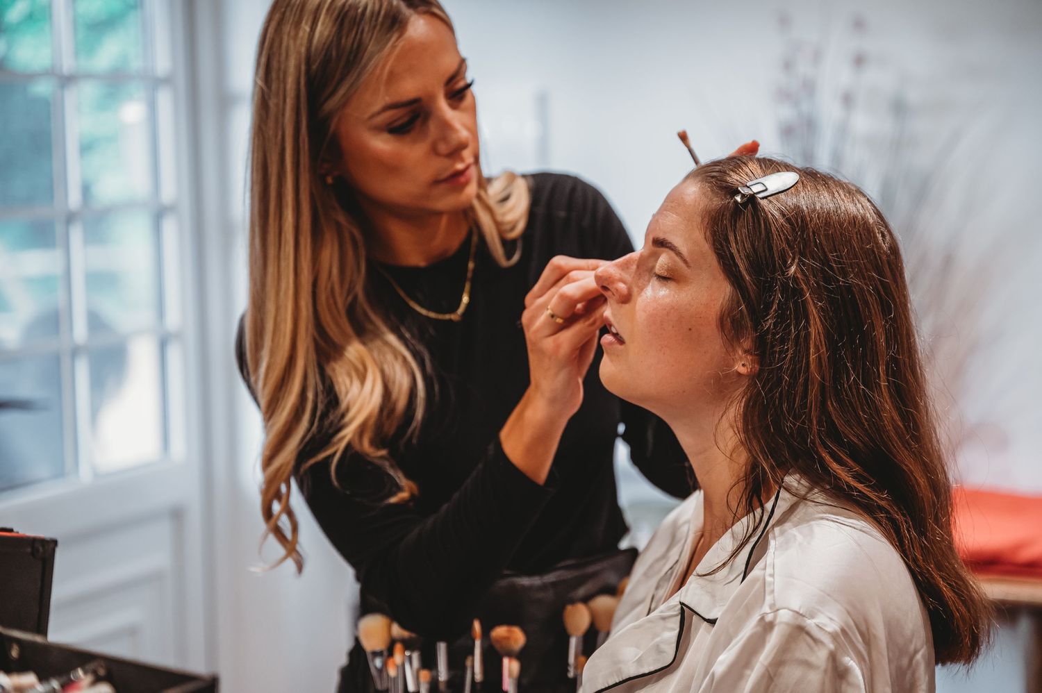 Professional makeup artist applying cosmetics to client in a bright studio setting.