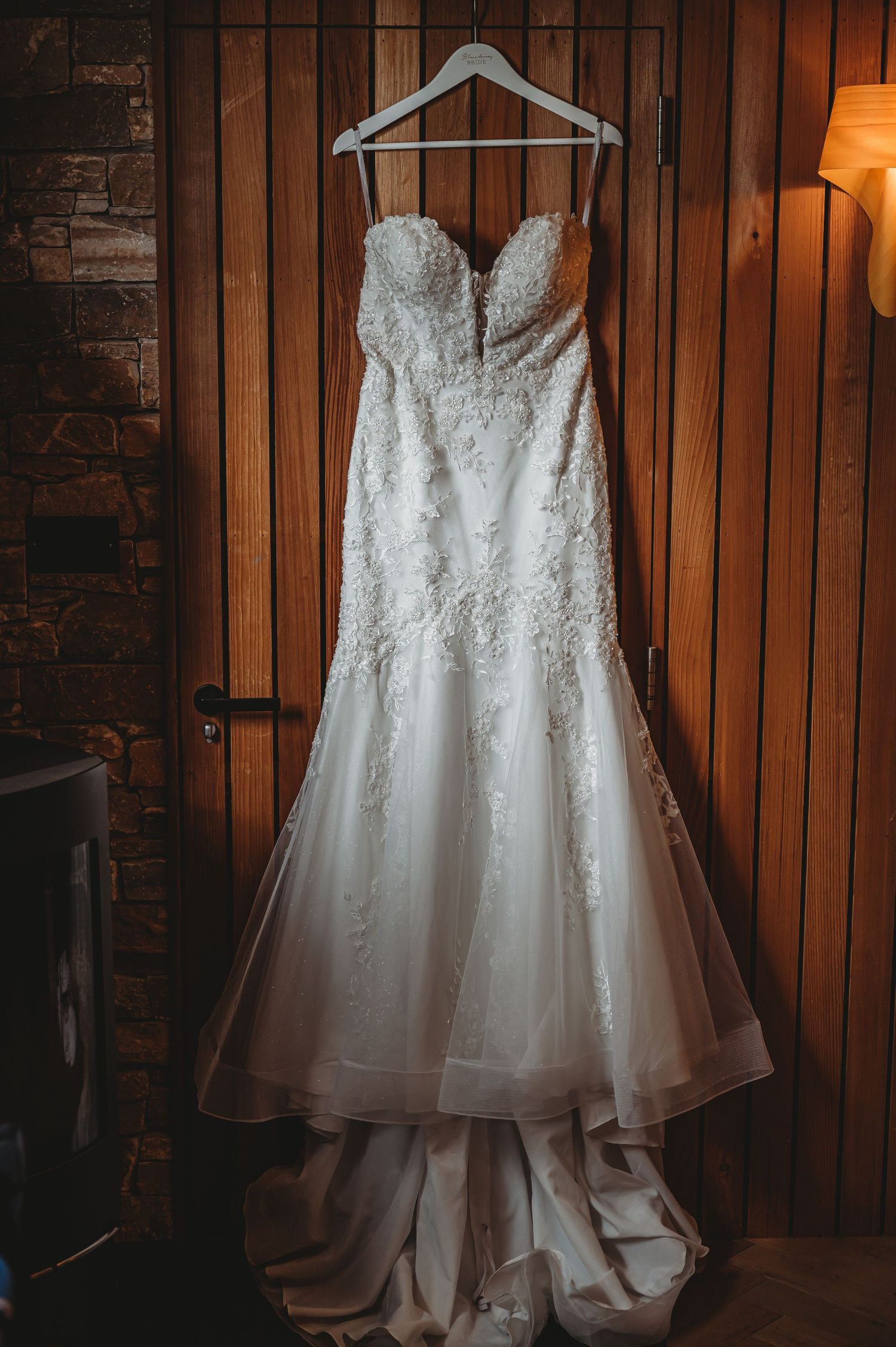 A beautiful white lace wedding dress with sweetheart neckline and fitted mermaid silhouette hangs elegantly on a hanger.