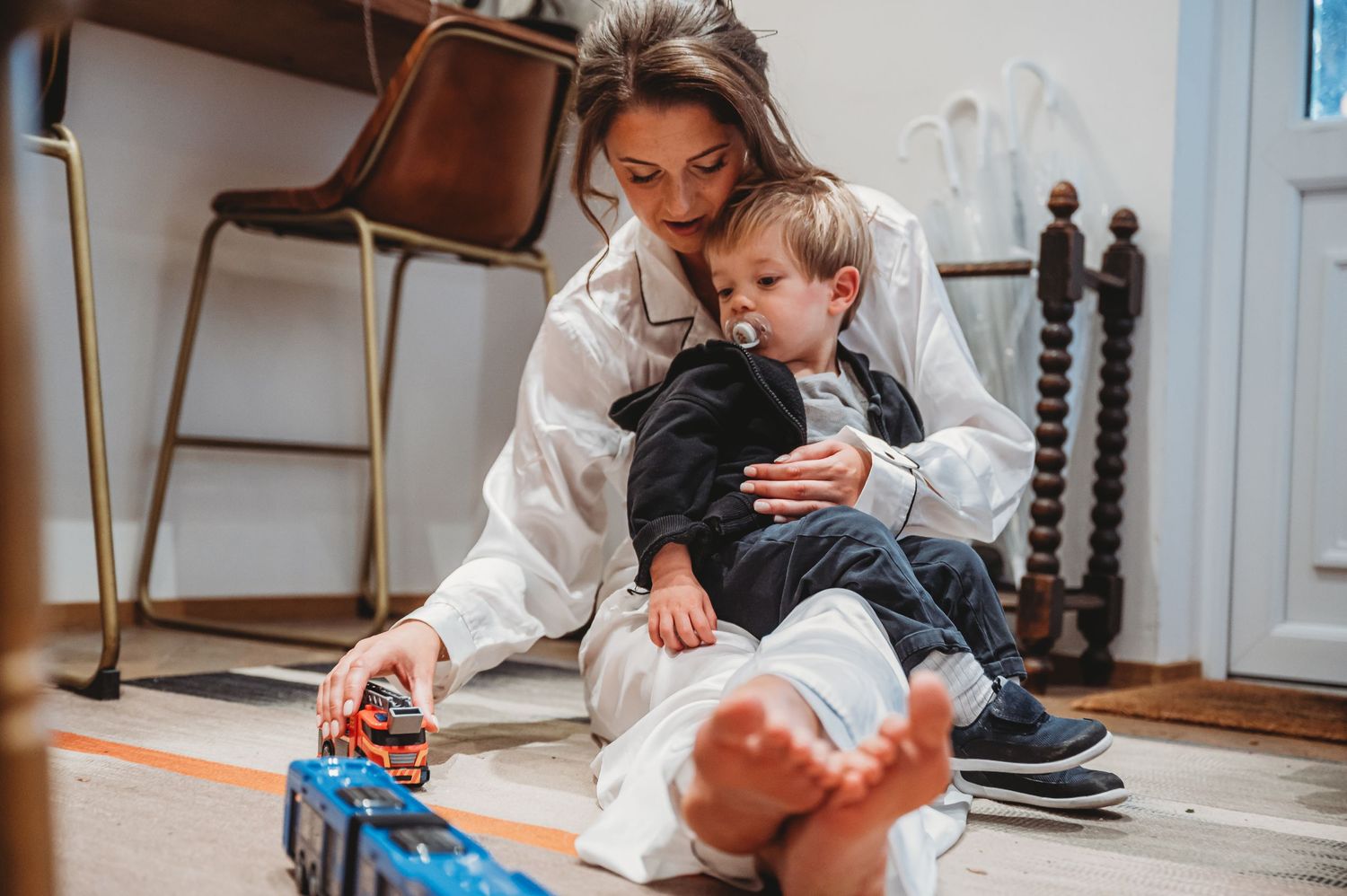 A parent and child playing with toy cars on the floor in a casual home setting.