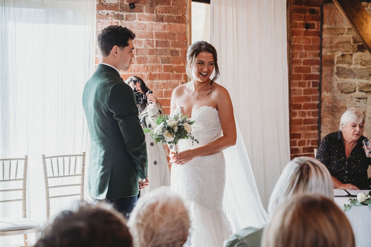 Wedding ceremony in rustic brick venue with white chairs and floral decorations.