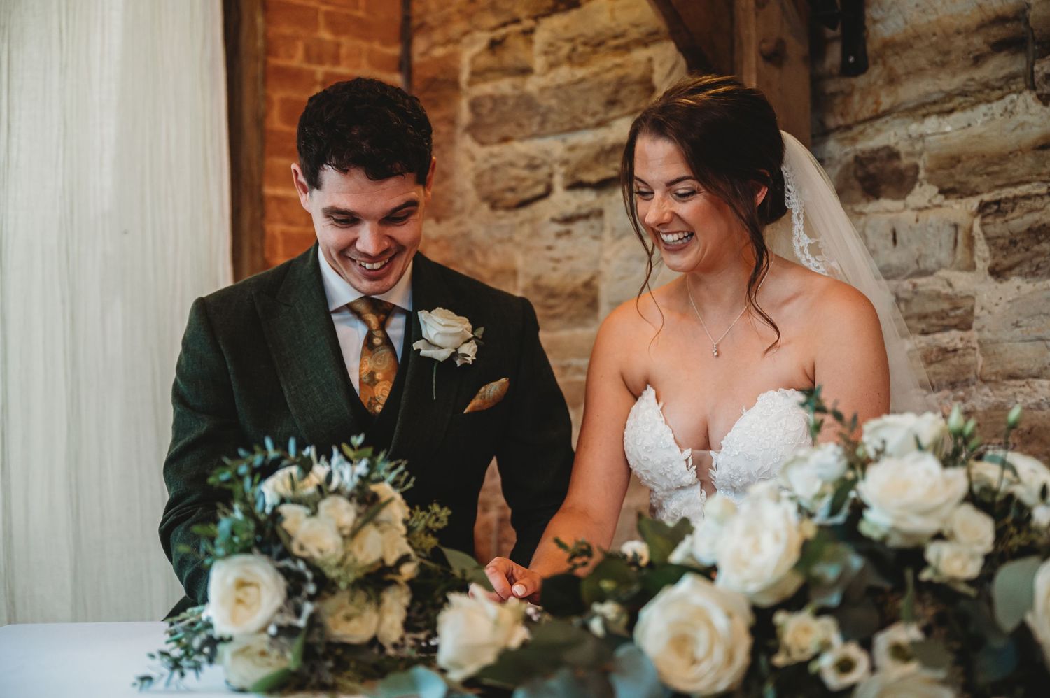 Couple shares joyful moment at reception table decorated with white roses and greenery.