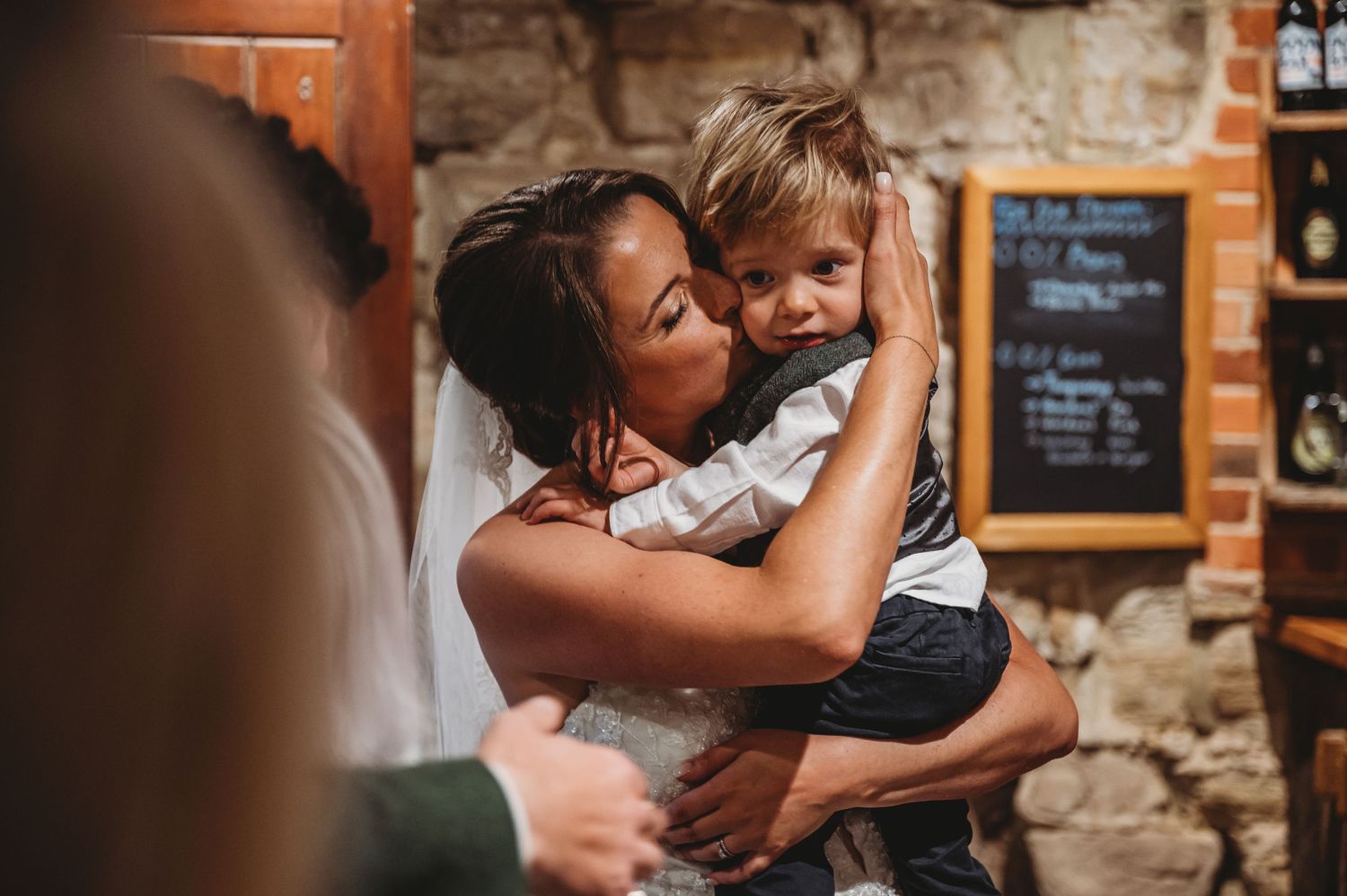 Emotional embrace during wedding reception in rustic venue with stone walls.