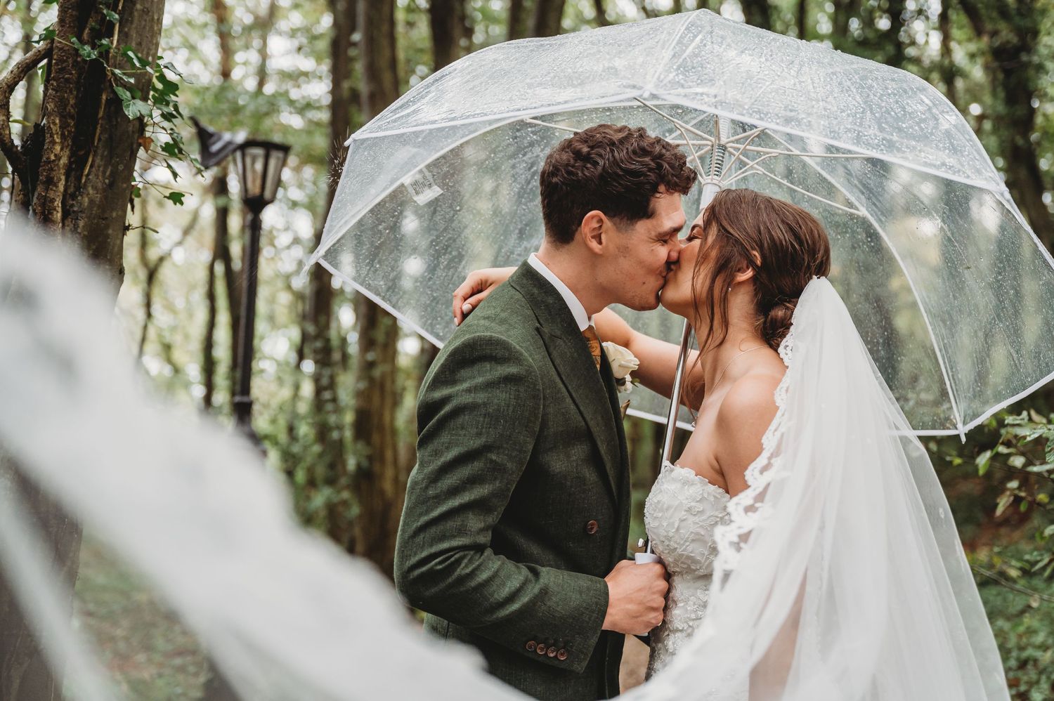 Romantic wedding portrait under a clear umbrella in a misty forest setting.