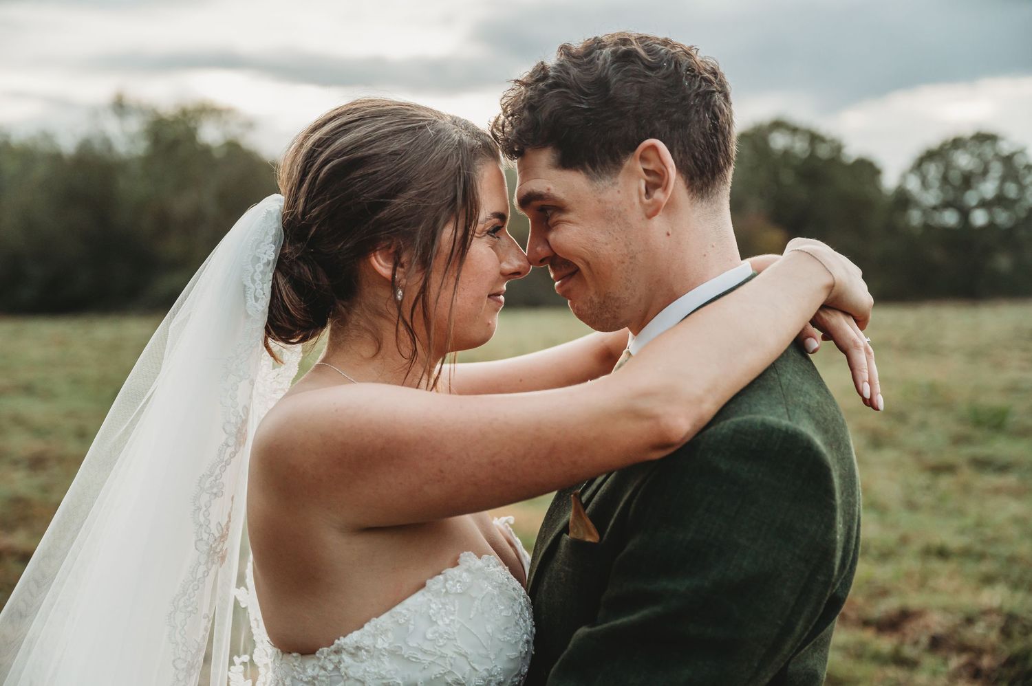 Romantic outdoor portrait of newlyweds embracing in a sunlit field.