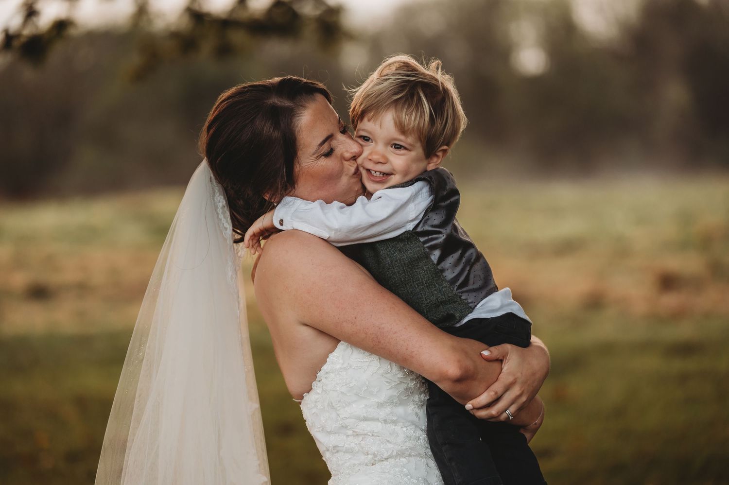 Tender moment captured outdoors in wedding attire against a natural backdrop.