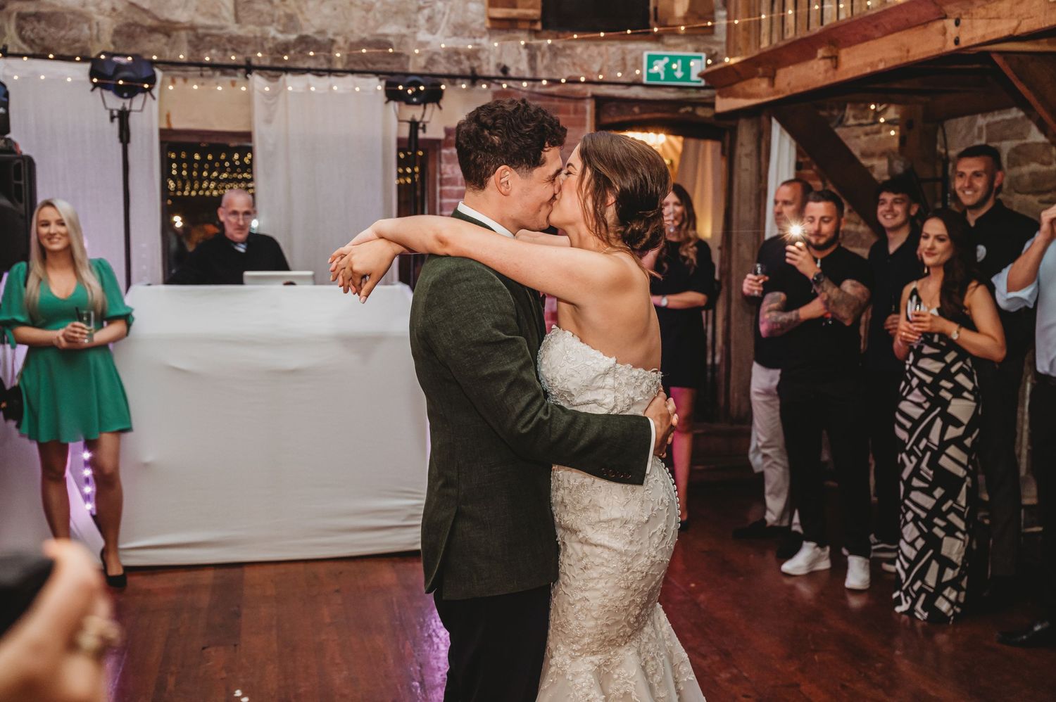 Newlyweds dance together surrounded by applauding wedding guests in an elegant indoor venue.