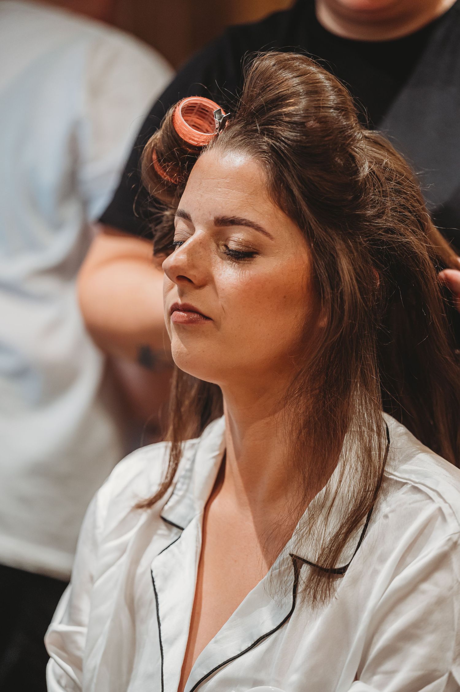 Side profile of someone getting their hair styled while sitting in a white robe with eyes closed.