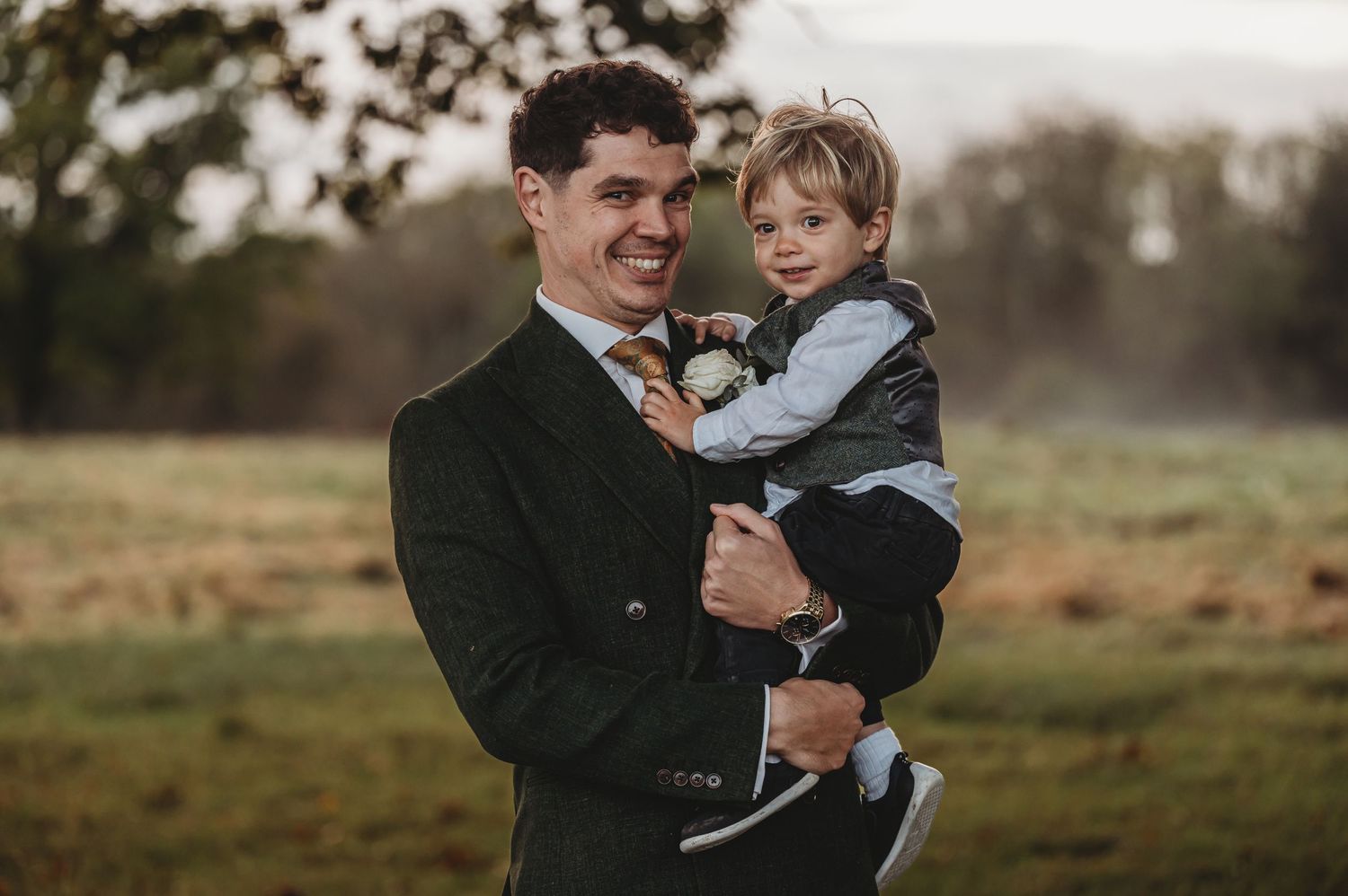 A parent and child share a joyful moment together outdoors in a natural field setting at dusk.