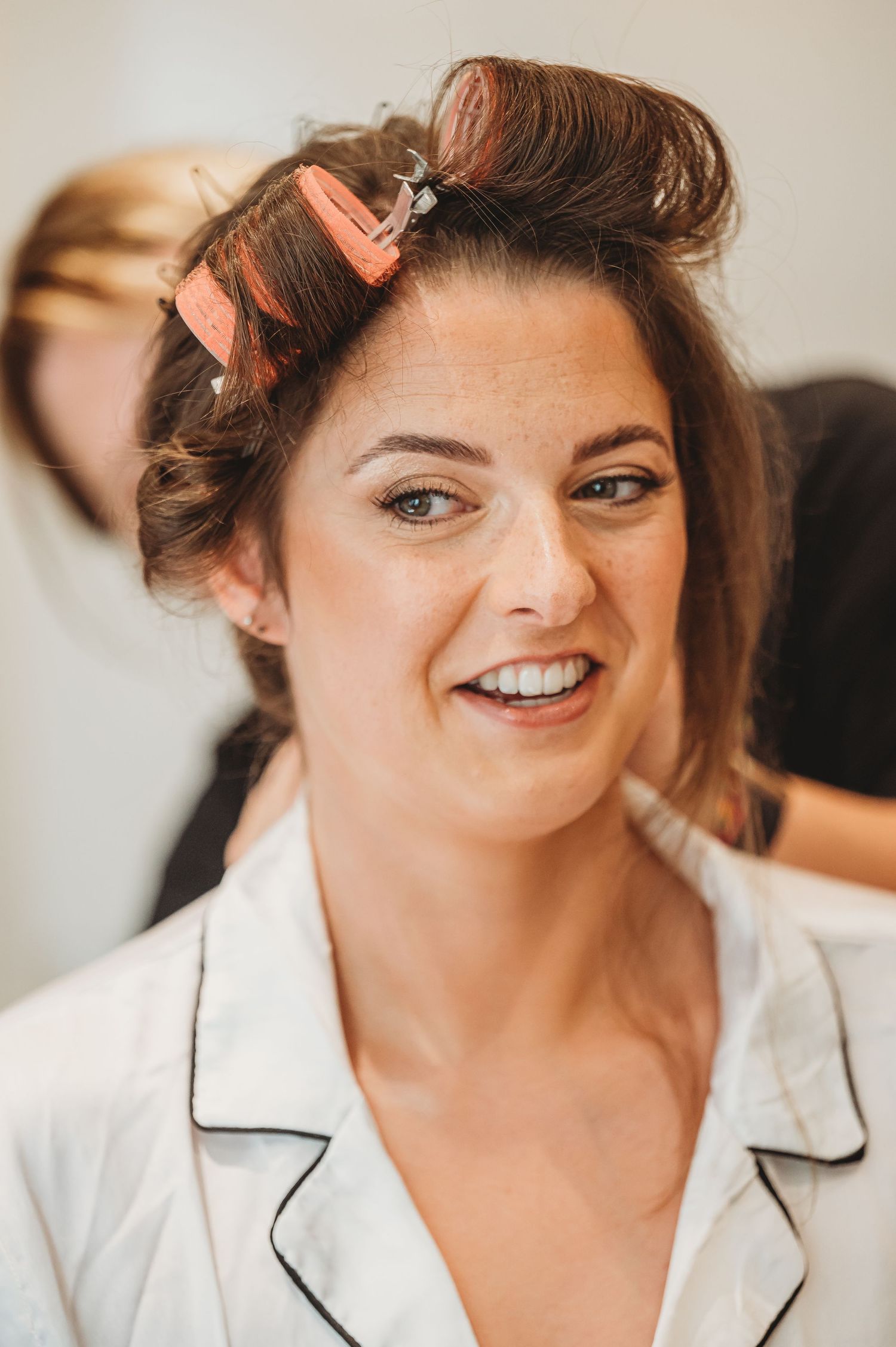 A styled portrait of someone in a white robe with coral hair rollers getting ready.